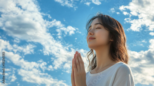 Young asian woman praying to god, thankful and grateful spiritual lady, christian religion or faith. blessed and hopeful in her belief,standing outdoors on a sunny day,blue sky,mental health, positive