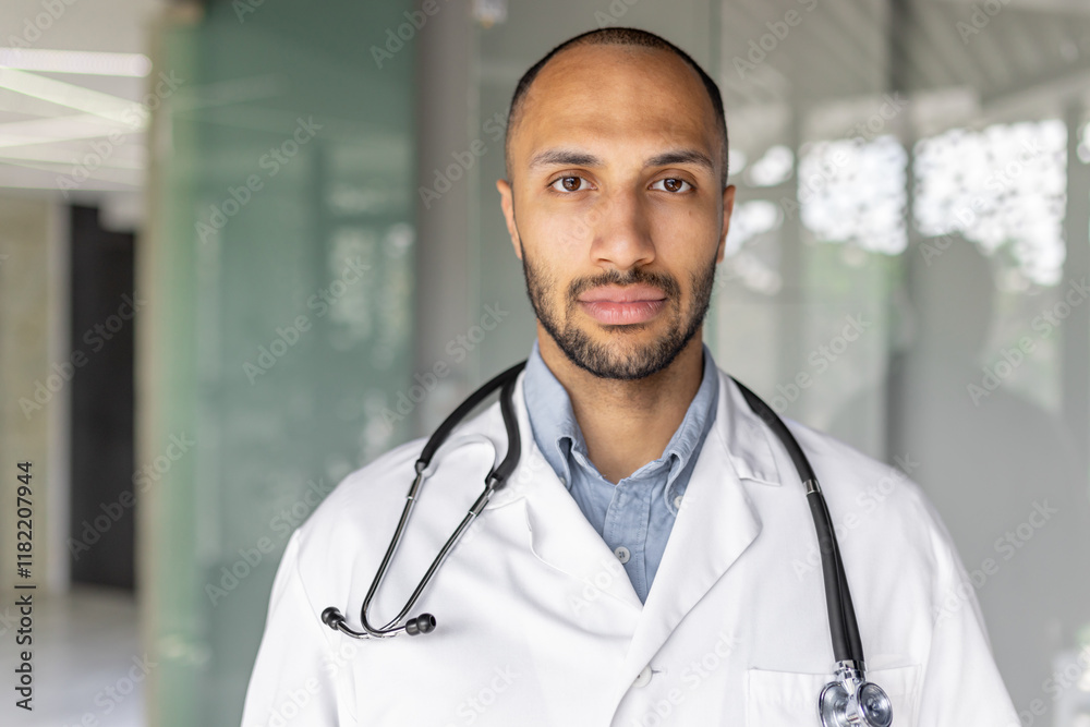 Close-up portrait of a doctor in a white medical coat, a man looks seriously and focused at the camera, the doctor works inside the clinic office at his workplace. Close-up portrait of a doctor in a white medical coat, a man looks seriously and focused at the camera, the doctor works inside the clinic office at his workplace.