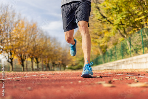 Fotografi Close up of male runner in sportswear sprinting on red track lane at outdoor stadium during training session