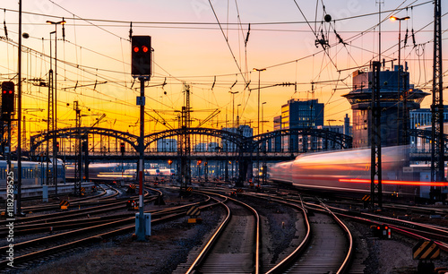 Fast trains leaving and arriving at Munich main station (Germany) in warm evening light. Blurred light traces. Railway infrastructure, signals, glistening tracks, switches. Long exposure at sunset.