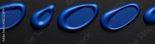 Blue paint drops on black background: A row of vibrant blue paint drops, each with a unique shape, lay gracefully against a stark black background.