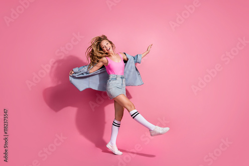 Joyful young girl in denim and pink showcasing trendy outfit on pink background photo