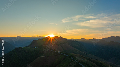 Aerial view of serene sunset casts a golden glow over rolling hills and distant mountain peaks, creating a peaceful and atmospheric landscape with layers of mist and soft light. mountain background..