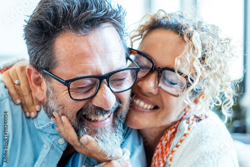 An adult couple in their late 40s, wearing glasses, smiling and embracing each other with joy while looking at the camera, enjoying a positive moment of their married life, filled with love and happy