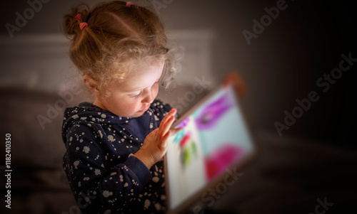 Obraz na płótnie Child playing on a tablet while sitting on a bed in the evening. w salonie