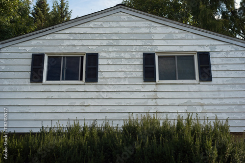 Detail of peeling paint on the aluminum siding on the upper level of a split-level house