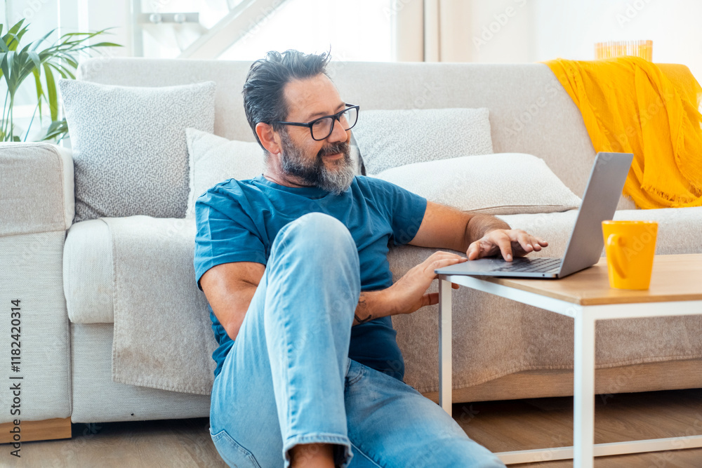 Man sitting comfortably on the floor in his apartment with a laptop placed on a small table, browsing the web to find interesting content, engaging with social media, and working remotely Man sitting comfortably on the floor in his apartment with a laptop placed on a small table, browsing the web to find interesting content, engaging with social media, and working remotely