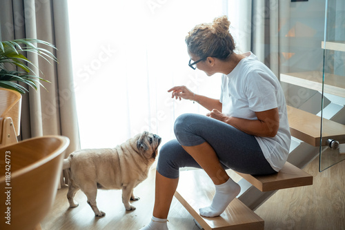 Woman alone in her living room, cuddling a pug on her lap, enjoying a peaceful afternoon moment with her pet, smiling while petting the dog and feeling a connection with her furry friend photo