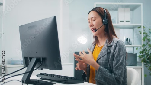 Professional Asian Female IT specialist engages with a customer, using headset and computer, talking with client instructions for solving technical problems sit at desk in modern call center office.