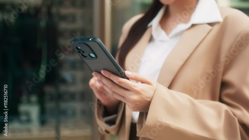 Close up of Asian businesswoman hand using a smartphone to browse the internet, typing a message standing outdoors office building. Asian woman worker using mobile phone device, working outdoors.