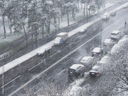 Obraz na płótnie View from the window over heavy fluffy snow falling over the street with cars parked along the roadside and urban park with green grass on a snowy winter day in Kyiv, Ukraine. w salonie