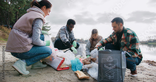 People finished bringing trash to one location. Starting placing everything into specific bags. Sorting out rubbish for future recycling. Helping each other. Teamwork concept. Man looking at camera.