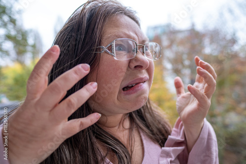 Angry mature white woman 50 years old with long hair expressing stress and frustration in natural outdoor setting, reacting with anger and tension photo