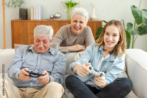 Happy family at home. Old senior man grandfather woman grandmother girl granddaughter playing video game with joysticks at home. Grandparent teenager two generations using gamepads for video game photo