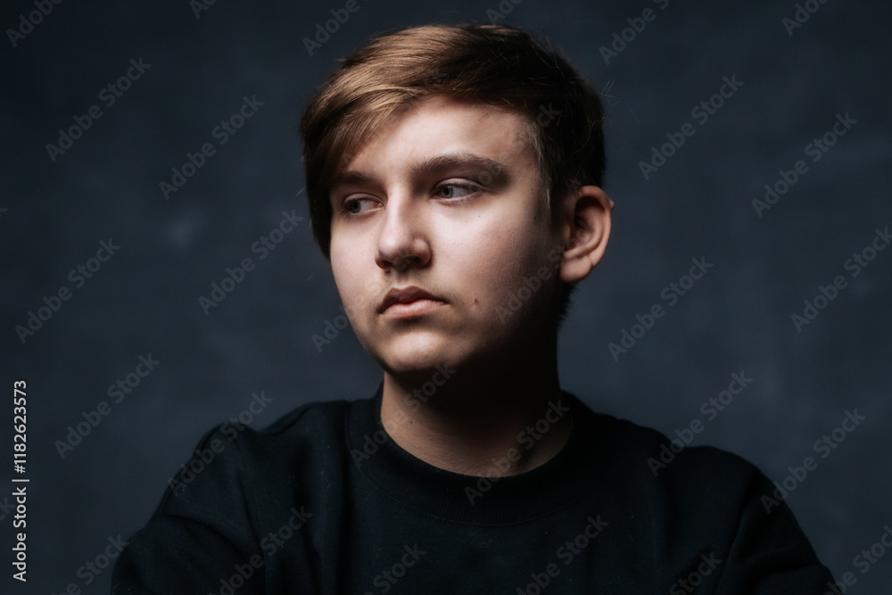 A close-up studio portrait of a young man in a black sweater, looking to the side with a calm and thoughtful expression. Soft lighting emphasizes his features against a dark background. A close-up studio portrait of a young man in a black sweater, looking to the side with a calm and thoughtful expression. Soft lighting emphasizes his features against a dark background.