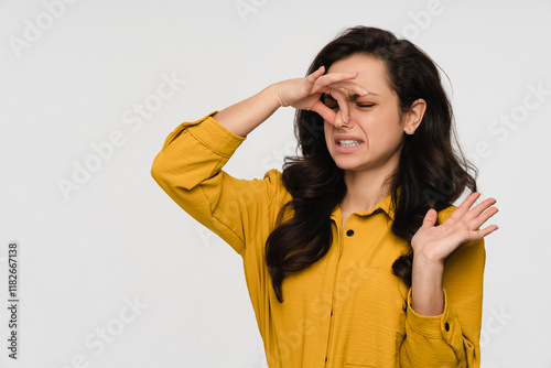 Beautiful young woman girl in casual clothes and long brown hair smelling stinky, closing her nose with a hand because of odor stench isolated in white background, copy space photo