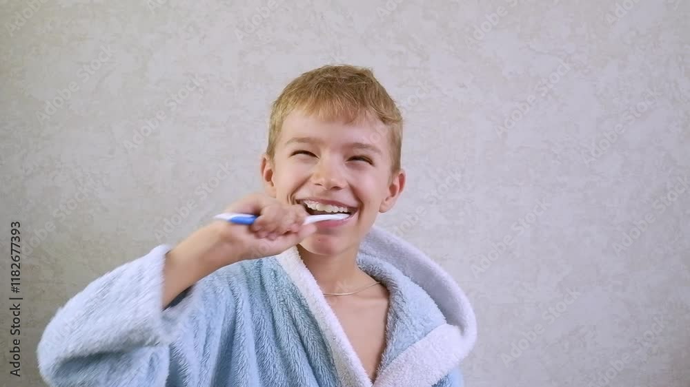 A child brushes his teeth. Children's toothbrush and toothpaste. A little boy in a blue robe brushes his teeth and laughs, fooling around. Oral hygiene and children's health. A child brushes his teeth. Children's toothbrush and toothpaste. A little boy in a blue robe brushes his teeth and laughs, fooling around. Oral hygiene and children's health.