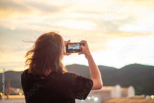A man takes a picture of a picturesque sunset on his smartphone.