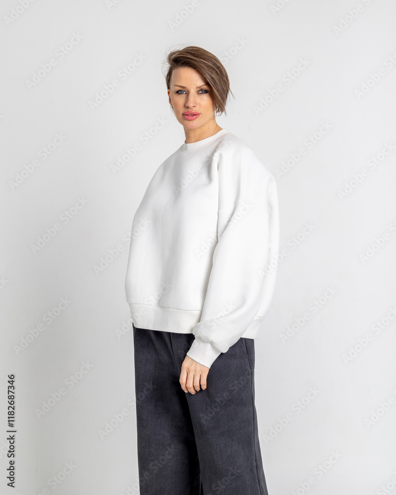 Portrait beautiful woman of model appearance. Girl in white sweatshirt, black trousers, on grey background. Pretty female with trendy makeup posing in studio. Vertical photo. Portrait beautiful woman of model appearance. Girl in white sweatshirt, black trousers, on grey background. Pretty female with trendy makeup posing in studio. Vertical photo.