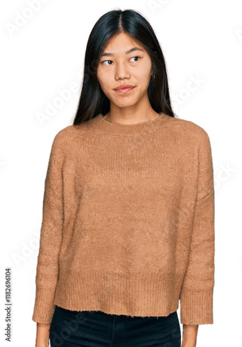 Beautiful young asian woman wearing casual winter sweater smiling looking to the side and staring away thinking.