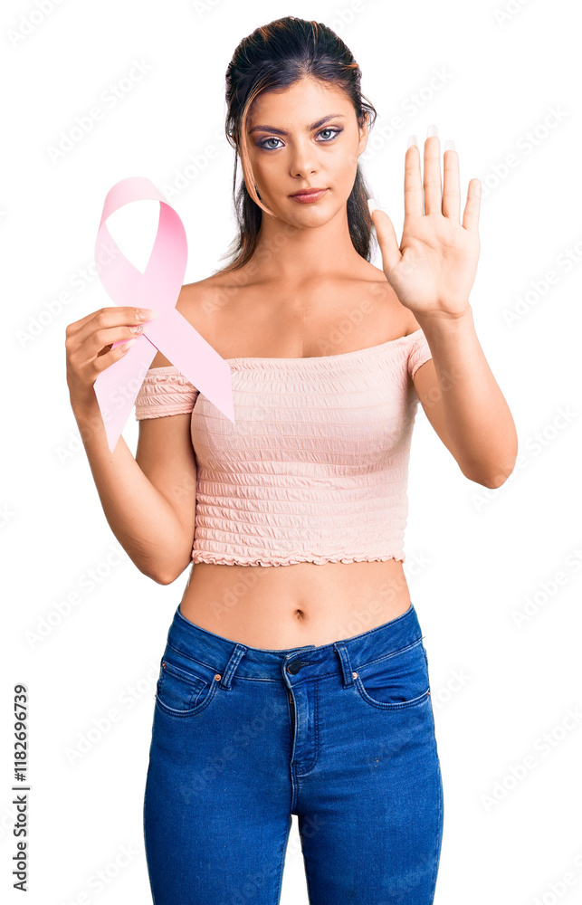 Young beautiful woman holding cancer awareness pink ribbon with open hand doing stop sign with serious and confident expression, defense gesture Young beautiful woman holding cancer awareness pink ribbon with open hand doing stop sign with serious and confident expression, defense gesture