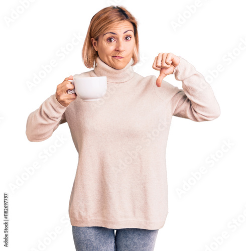 Young blonde woman holding coffee with angry face, negative sign showing dislike with thumbs down, rejection concept