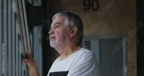 Elderly man leaning on metal bars, gazing at and surveilling the street from a garage in isolation at home, capturing a moment of reflection, solitude, and thoughtfulness photo