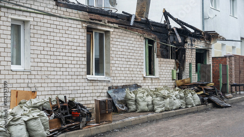 A private home stands in ruins after a devastating fire, with charred belongings scattered on the street. The scene reflects the aftermath of destruction and loss, evoking deep emotions.