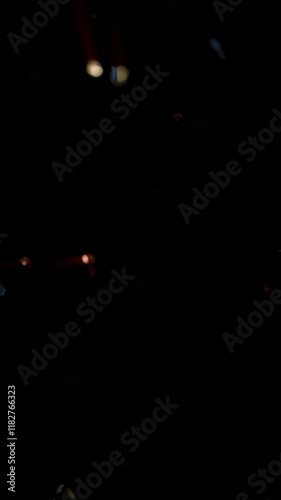Vertical Glitter Confetti Flight on Black 4K Loop features multicolored confetti falling with light beams emanating from the highlights against a black background in a vertical ratio loop.