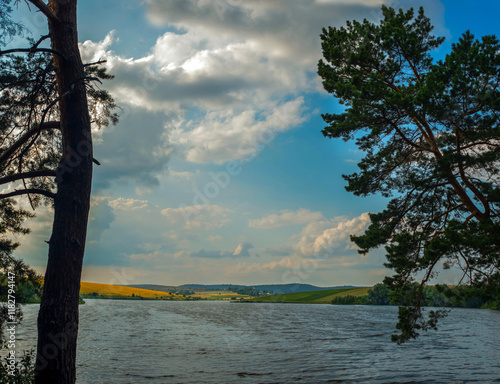 scenic view from the shore with pine trees silhouettes to the lake and rural ...