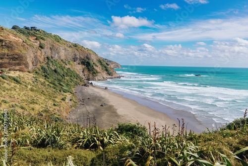 Coastal scene of a black sand beach at Murawai. Waves crash on shore, with people visible on the beach. Sunny day with a clear sky.  Auckland, New Zealand photo