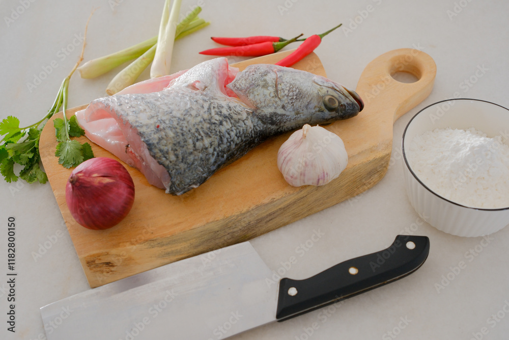 Fresh snapper fish on a wooden cutting board in a kitchen with a knife nearby