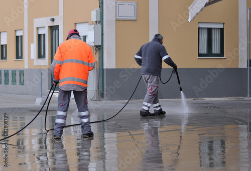 City street cleaning workers washing sidewalks with a water pressure gun