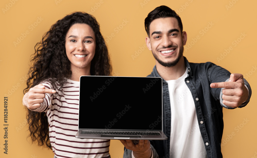Great Website. Smiling middle eastern couple pointing at laptop with black screen for mockup, demonstrating copy space for your web design and advertisement, standing isolated over yellow background Great Website. Smiling middle eastern couple pointing at laptop with black screen for mockup, demonstrating copy space for your web design and advertisement, standing isolated over yellow background