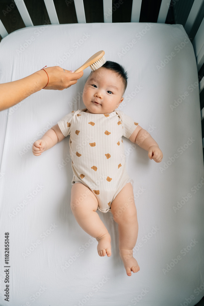 A mom brushes the baby's hair in the crib. A mom brushes the baby's hair in the crib.