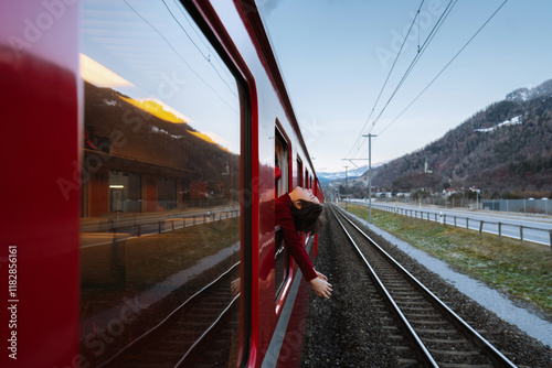 Teen woman with head and arms outside window of train