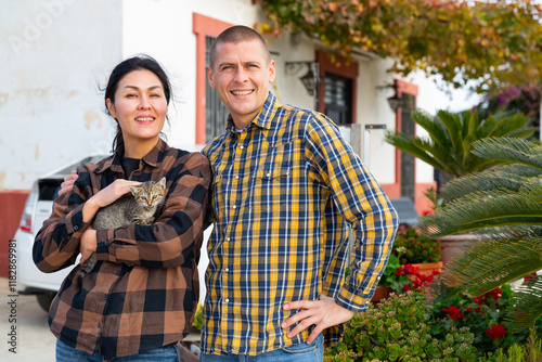 Obraz na plátně Smiling romantic american man and asian woman standing with their pets cats near