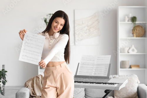 Young woman with note sheet and synthesizer at home