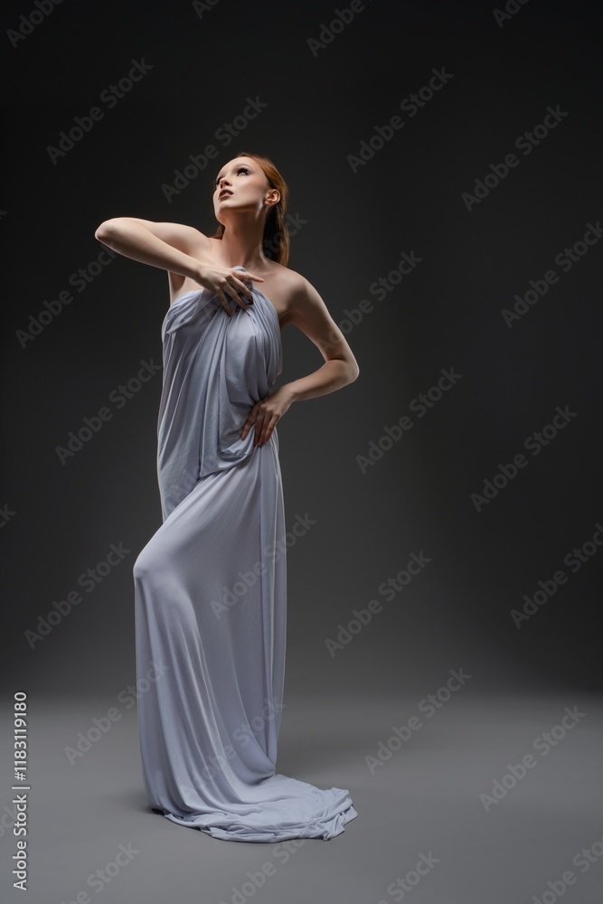 Fototapeta premium Elegant woman in a flowing dress poses dramatically in a dimly lit studio