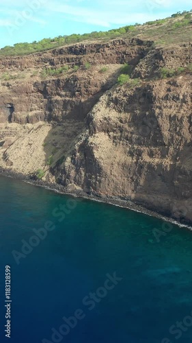 An aerial view of steep rocky coastal cliffs meeting calm blue ocean waters, showcasing the rugged beauty of Captain Cook, Hawaii. photo