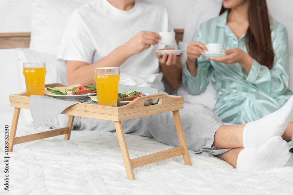 Young couple with cups of coffee having breakfast in bedroom Young couple with cups of coffee having breakfast in bedroom