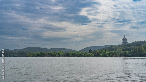 Beautiful calm lake. Ripples on the water. Green vegetation on the shore. On a hill, against the background of the sky and clouds, a tall pagoda is visible. China. Hangzhou. West Lake Xi Hu photo