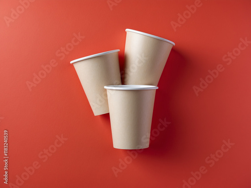 Three light beige disposable paper cups arranged on a vibrant red background, showcasing eco-friendly packaging, perfect for themes related to sustainability, beverages, and takeaway services. photo