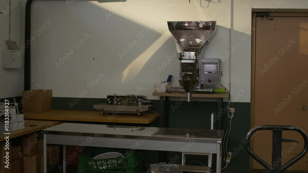 Medium long shot of big commercial coffee roasting or grinding machine in compact workspace surrounded by tools, tables and boxes, no people Medium long shot of big commercial coffee roasting or grinding machine in compact workspace surrounded by tools, tables and boxes, no people