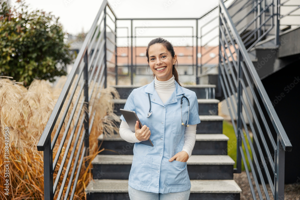 Smiling female doctor standing on stairs with tablet in hands and looking at camera. Smiling female doctor standing on stairs with tablet in hands and looking at camera.