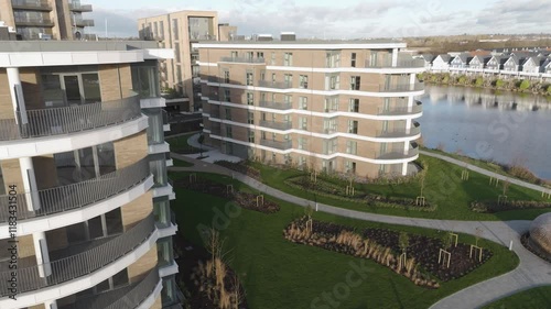 Aerial orbit of sleek lakeside flats with curved facades, manicured lawns, and a calm shoreline bathed in evening light photo