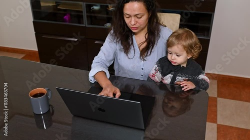 Mother working on a laptop with her child at the dining table