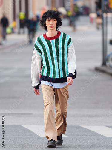 Portrait of a handsome Chinese young man with black and blue striped sweater walking in the street,  young guy with black curly hair in urban background. male fashion, cool Asian young man lifestyle.
