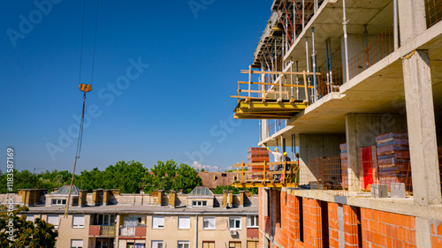 Photos Worker on scaffold is helping crane to manage pile red blocks packed in plastic