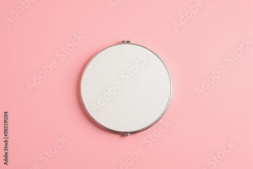 A compact pocket mirror with a polished surface on a pastel rose background
